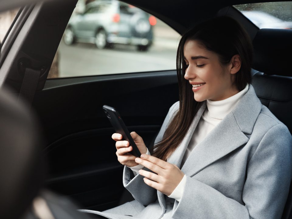 Uber ou 99? Saiba qual o melhor app para fazer suas viagens mulher sorridente viajando de carro