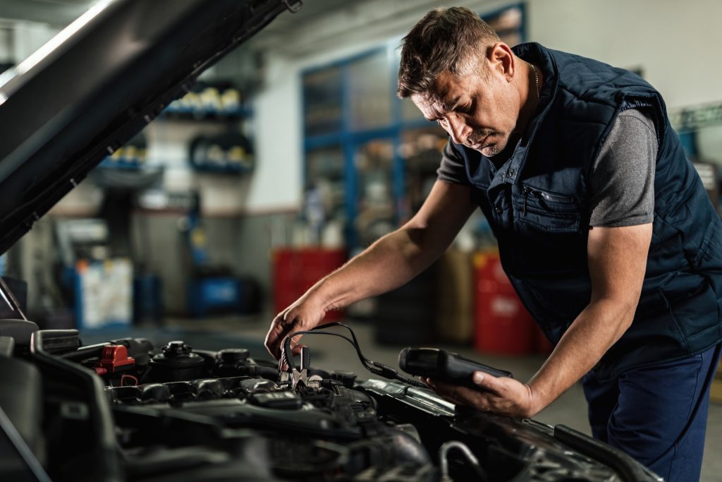 Dicas para Economizar na Manutenção e Reparos do seu Veículo auto mechanic using diagnostic tool while checking car battery voltage workshop